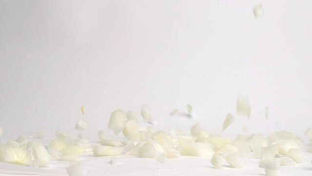 Diced white onion pieces falling and bouncing on white table top in slow motion