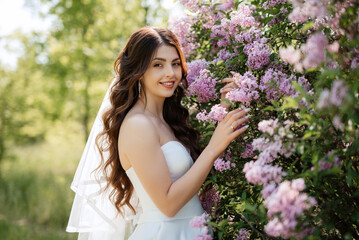 Fototapeta premium young girl bride in a white dress in a spring forest in lilac bushes