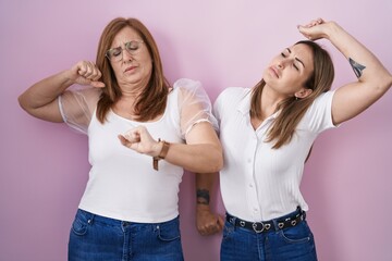 Hispanic mother and daughter wearing casual white t shirt over pink background stretching back, tired and relaxed, sleepy and yawning for early morning