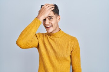 Young hispanic man standing over blue background surprised with hand on head for mistake, remember...