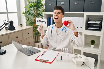 Young hispanic doctor man supporting organs donations angry and mad screaming frustrated and furious, shouting with anger looking up.