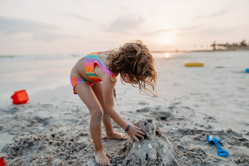 Little girl playing on the beach, building sand castle.