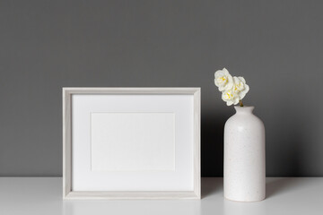 Blank picture frame mockup in minimalistic interior with vase decor with flowers