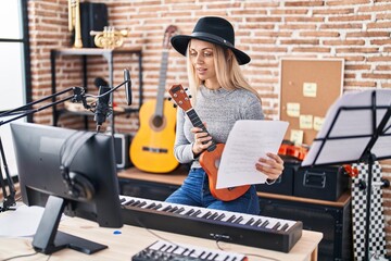 Young woman artist holding ukelele reading song at music studio