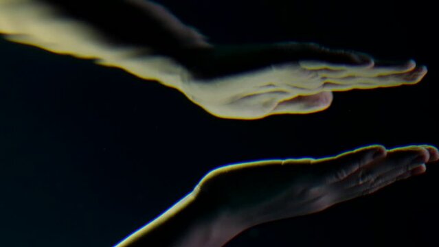 The hand reaches out from under the water to the sun rays. It is reflected in the mirror of the surface of water sinking in the sea or ocean and rising to the surface