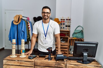 Young hispanic man shopkeeper smiling confident working at clothing store - obrazy, fototapety, plakaty