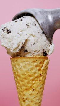 Vertical slow motion video, Scooping cookies and cream ice cream in a cone on pink background, delicious ice cream concept.