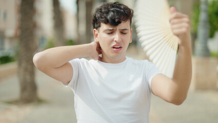 Naklejka premium Non binary man using handfan suffering for hot at park