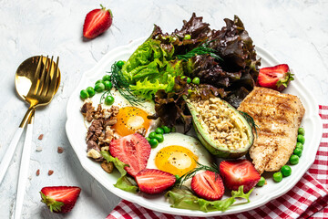 Healthy nutritious paleo keto breakfast diet Fried eggs, avocado, grilled chicken fillet, nuts, strawberries and fresh salad. Keto breakfast or lunch. top view