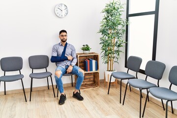 Young arab man sitting on chair with arm sling at clinic waiting room