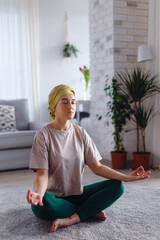 Young woman with cancer taking yoga and meditating in her apartment.