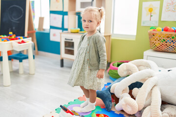Adorable blonde girl standing with relaxed expression at kindergarten