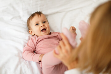 Baby gymnastics. Cute little baby girl enjoying massage from her mother, woman holding kid's legs and doing exercises