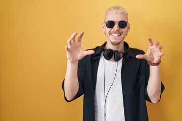 Young caucasian man wearing sunglasses standing over yellow background smiling funny doing claw gesture as cat, aggressive and sexy expression