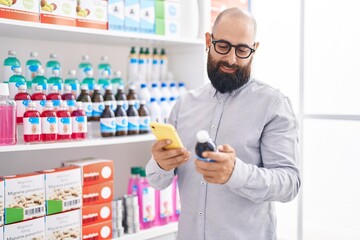 Young bald man customer using smartphone holding medicine bottle at pharmacy