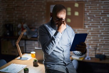 Young hispanic man with beard and tattoos working at the office at night tired rubbing nose and eyes feeling fatigue and headache. stress and frustration concept.