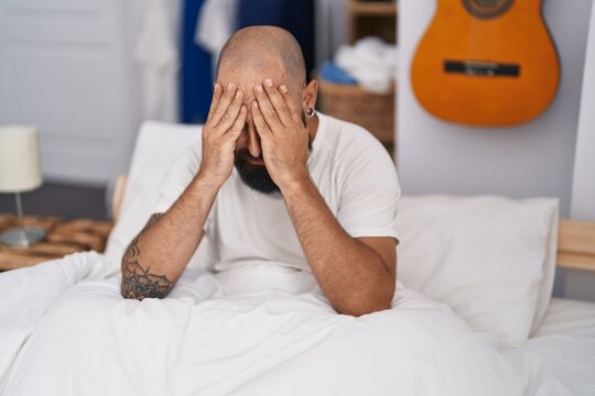 Young bald man stressed sitting on bed at bedroom