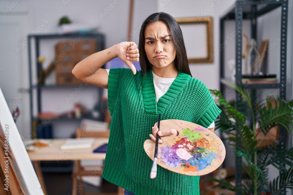 Canvas Prints Young south asian woman holding painter palette with angry face, negative sign showing dislike with thumbs down, rejection concept