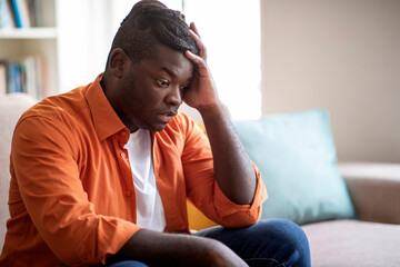 Shocked chubby black guy sitting alone on couch at home