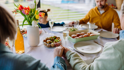 Close-up of family holding hands, praying before Easter lunch.