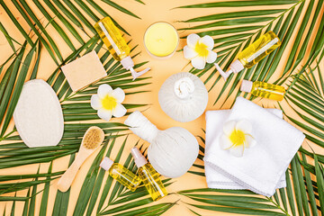 Spa massage Aromatherapy body care background. Spa herbal balls, cosmetics, towel and tropical leaves on orange table. Top view, flat lay, overhead, copy space. Beauty and health care concept