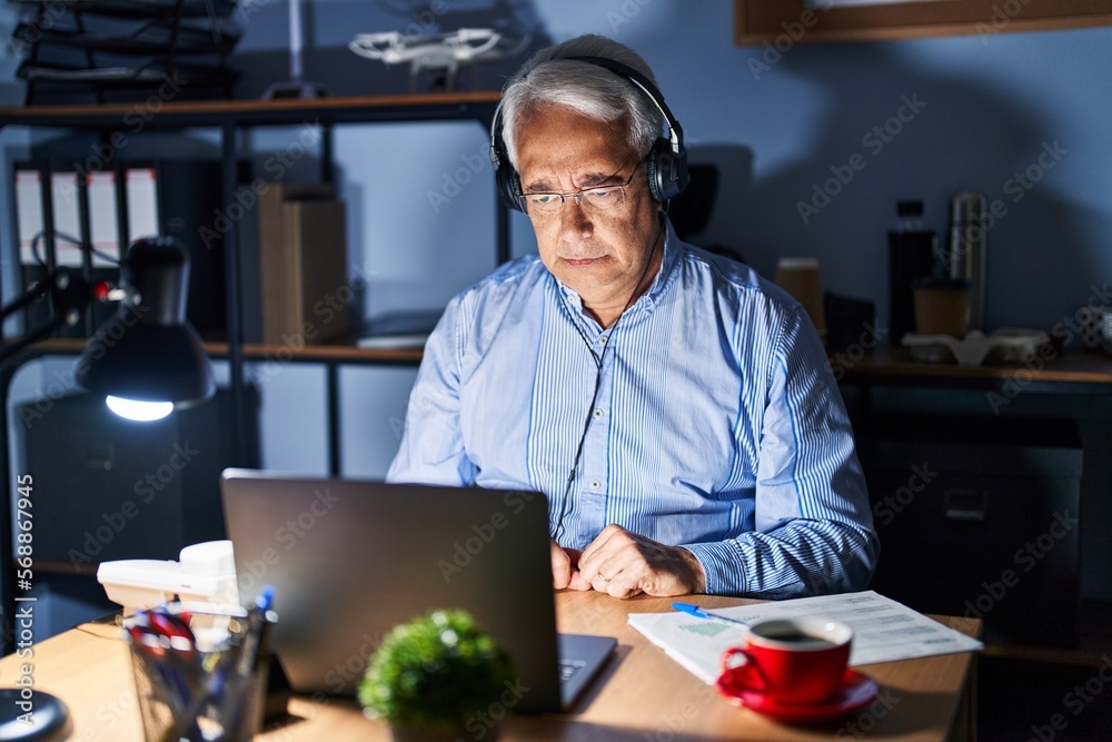 Wall mural Hispanic senior man wearing call center agent headset at night skeptic and nervous, frowning upset because of problem. negative person.