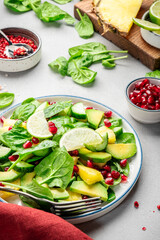 Avocado vegan salad with pineapple, spinach and pomegranate seeds, gray table, top view. Healthy eating, clean food, diet, weight loss concept