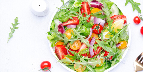Fresh spring vegan vegetables salad with colorful cherry tomatoes, cucumber, red onion, lettuce, radicchio and arugula. White table background, top view