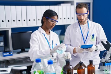 Fototapeta premium Man and woman scientists using touchpad measuring liquid at laboratory