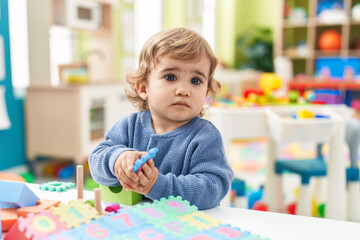 Adorable hispanic toddler playing with construction blocks standing at kindergarten