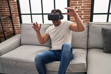 Young hispanic man playing video game using virtual reality glasses at home
