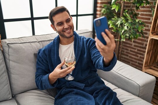 Young hispanic man make selfie by smartphone drinking wine at home