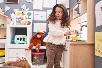 Adorable hispanic girl playing with play kitchen standing at kindergarten