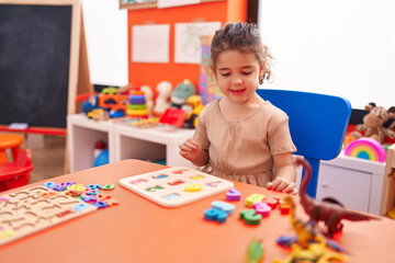 Fototapeta premium Adorable hispanic girl playing with maths puzzle game sitting on table at kindergarten