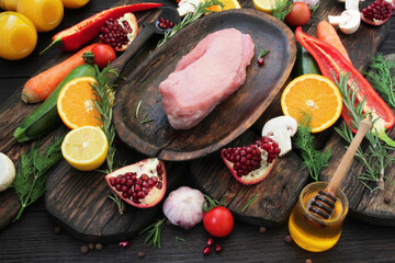 Fresh, pink, pork pulp on a wooden plate and on a wooden table, spices, herbs, vegetables and fruits with marinade are carefully laid out around the pork.