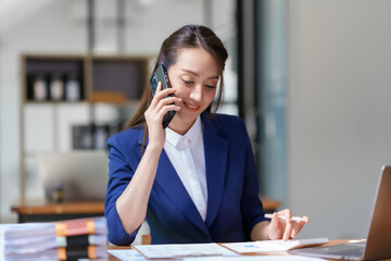 Beautiful smiling Asian businesswoman talking on mobile phone while working in office.