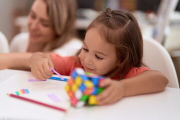 Obraz na płótnie Canvas Teacher and toddler sitting on table holding rubik cube at kindergarten