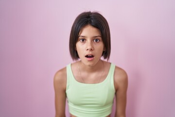Young girl standing over pink background afraid and shocked with surprise and amazed expression, fear and excited face.