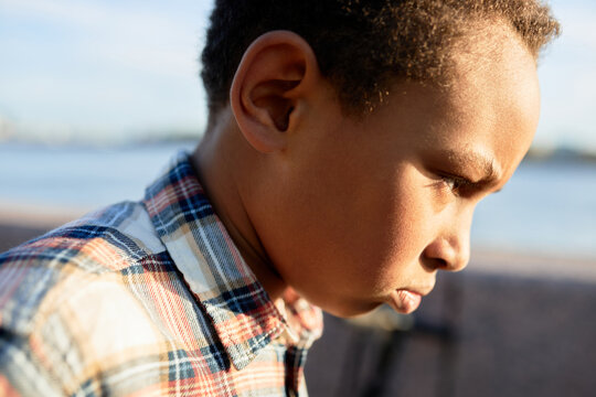 Outdoor profile view image of angry african american frustrated offended boy kid walking quickly in city street after quarrel with his mom or friends. Children, their emotions and facial expressions