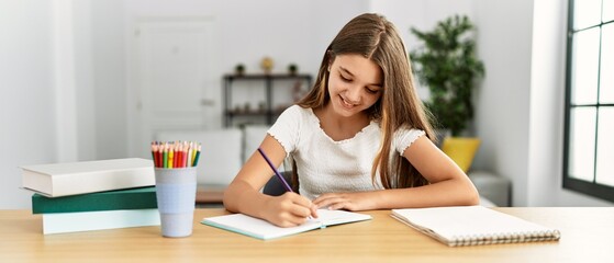 Adorable girl doing homework sitting on table at home