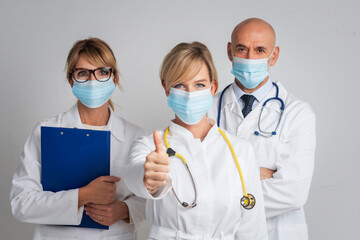 Female medical worker wearing face mask and showing thumbs up while standing together with her team