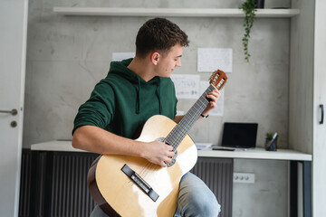 Obraz premium One young man Caucasian teenager sit at home in room playing guitar
