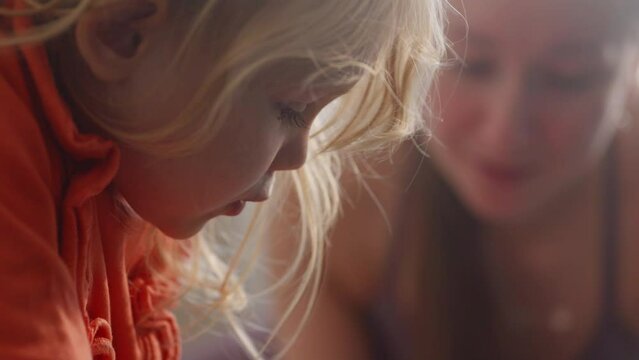 Close up view of baby girl learning how to read a book with mothers help, spending time together. Interested kid studying new things. Mom and daughter family time. High quality 4k footage