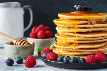 Delicious pancakes, with fresh blueberries, raspberry and maple syrup or honey on a dark background