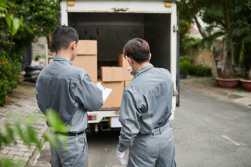 Movers checking document and counting boxes loaded in truck