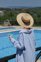 Back view of relaxed young woman enjoying hot day, having margarita cocktail at the swimming pool....