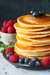 Delicious pancakes, with fresh blueberries, raspberry and maple syrup or honey on a dark background