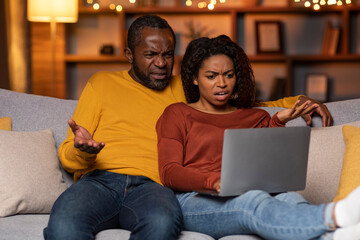Furious black couple looking at laptop screen, reading news online
