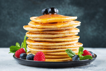 Delicious pancakes, with fresh blueberries, raspberry and maple syrup or honey on a dark background