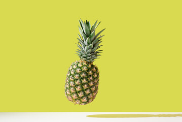 Una piña entera suspendida en el aire contra una pared amarilla	